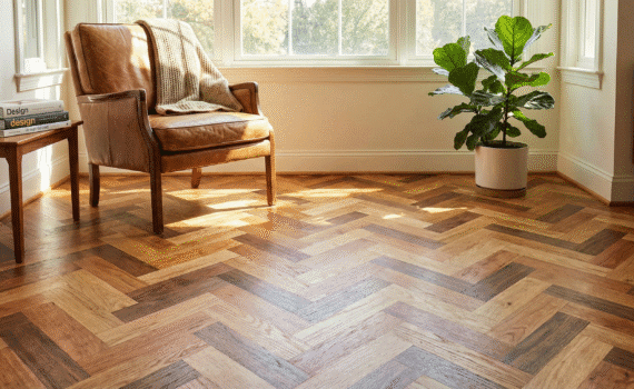 "Ambiente de sala de estar sofisticada com luz solar incidindo sobre um piso de tacos de madeira maciça instalado em paginação espinha de peixe, mostrando variações de tons naturais. Uma poltrona de couro e uma planta complementam a decoração acolhedora, ilustrando a durabilidade e estética dos produtos Monet Decor."